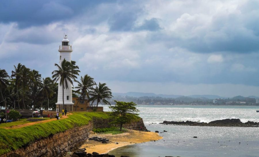 The white lighthouse on the Galle fort ramparts above the beach, with palms and the sea beyond