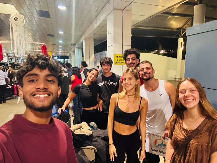 A group of seven travellers with their driver-guide outside the airport terminal at night, just after landing