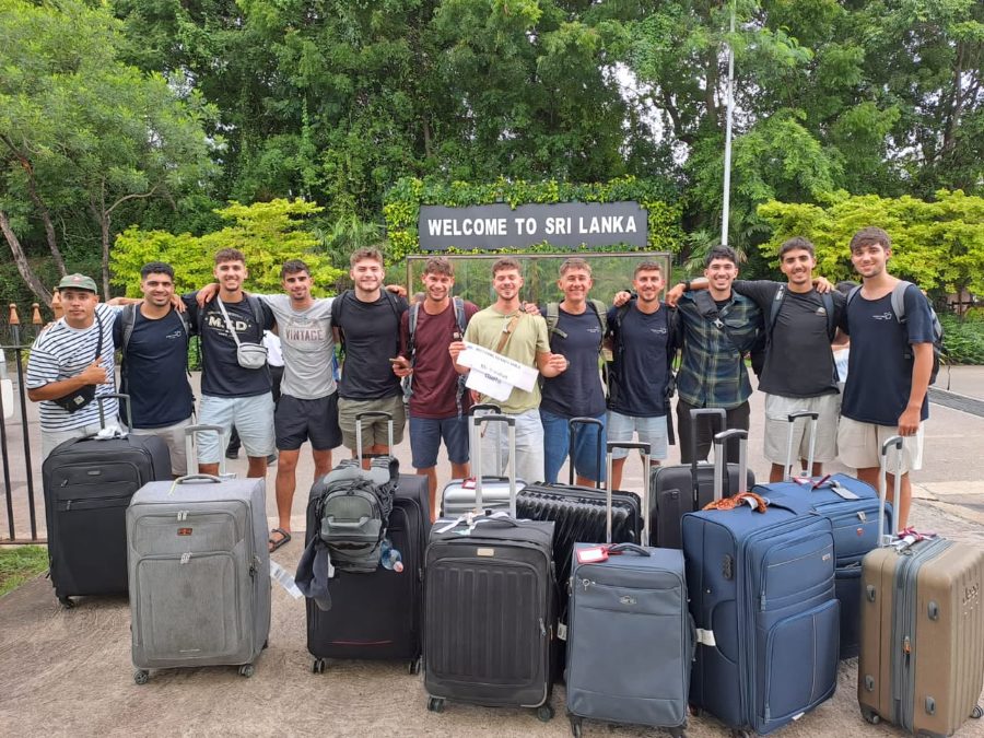 A large group of travellers with their luggage under the Welcome to Sri Lanka sign at the start of their trip